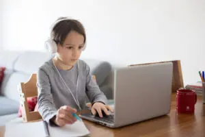 School child, sitting at the table with laptop, writing school tasks while homeschooling, while school closed due to Coronavirus