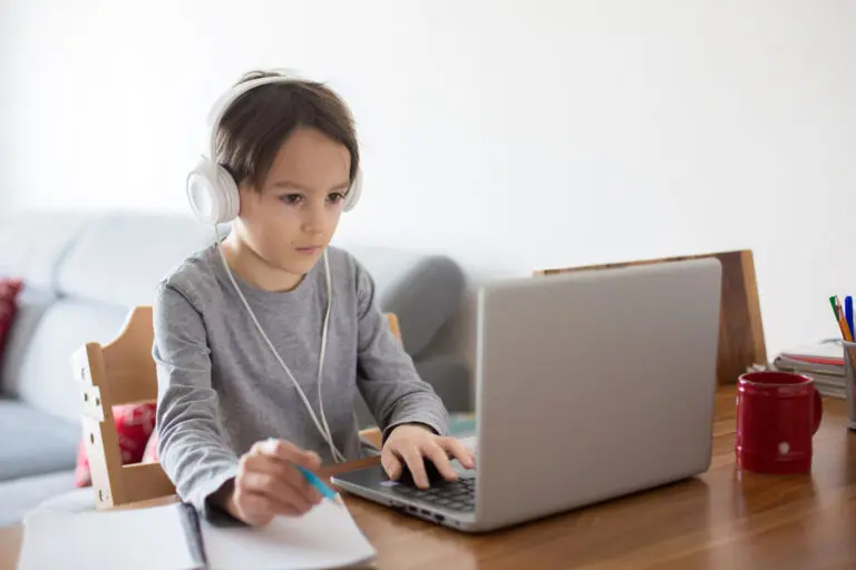 School child, sitting at the table with laptop, writing school tasks while homeschooling, while school closed due to Coronavirus